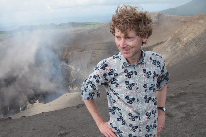 Clive Oppenheimer posing beside smoking volcano
