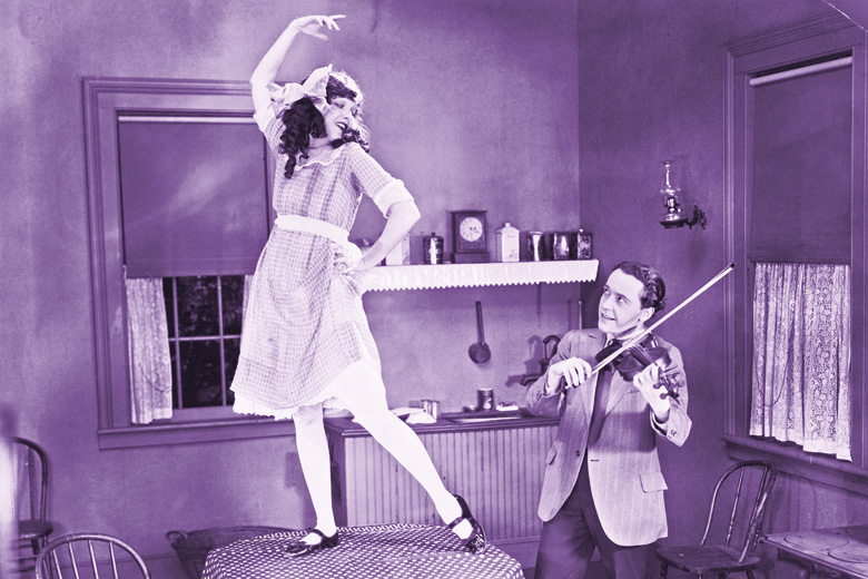 Husband playing violin while wife dances on table