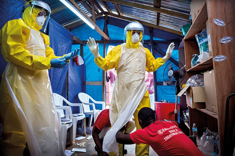 Western aid workers are helped into their PPE by two local staff at an ebola treatment centre in Sierra Leone