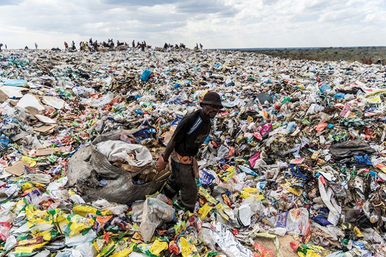 A recycler drags a bag of paper past a heap of non-recyclable material at a sanitary landfill site in Bulawayo, Zimbabwe