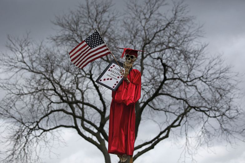 Skeleton in an academic gown holding a flag and placard