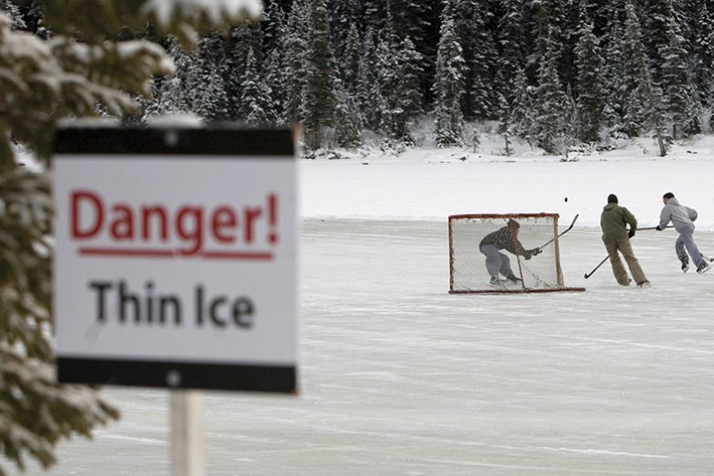 A group of skaters play pond hockey on Lake Louise, with a "Danger! Thin ice" sign.