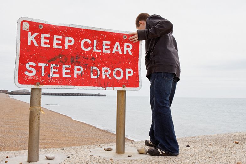 Person near edge with "Keep Clear. Steep drop" sign