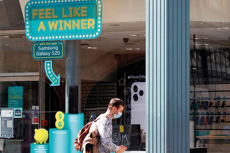 pedestrian, wearing a protective mask, walks past a window with feel like a winner sign.
