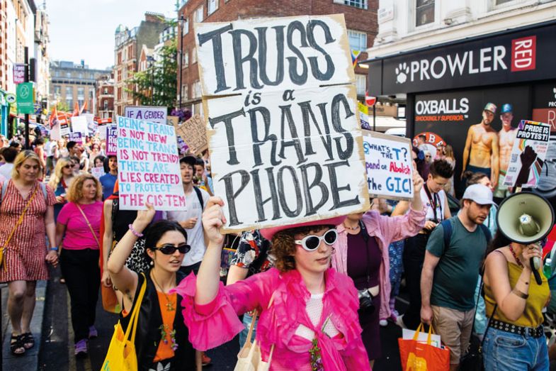 Protester holding banner reading 'Truss is a transphobe' during a protest as described in the copy