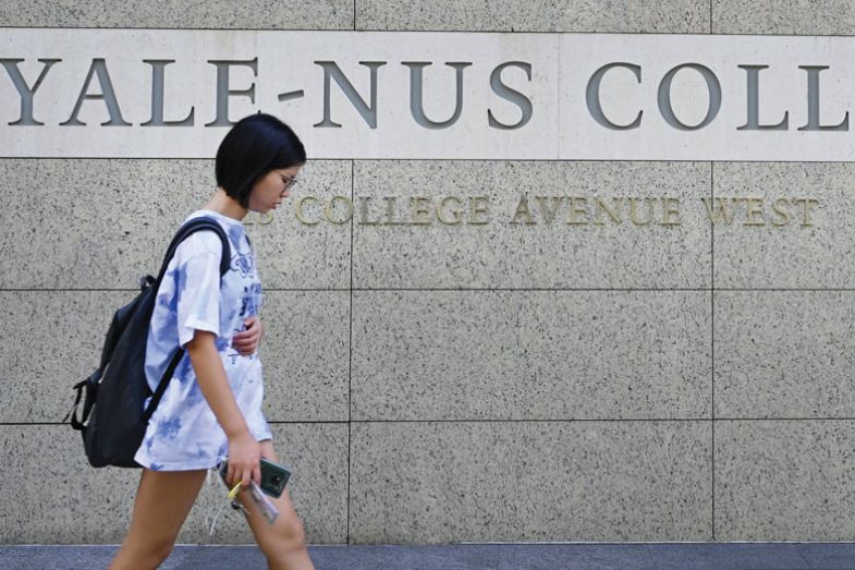 A student walking past signage for the Yale-NUS College in Singapore as described in the article