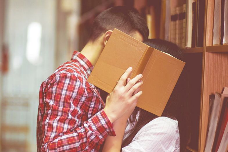 Photo of man and woman kissing in library and close their face by book for Getting back to the stacks.