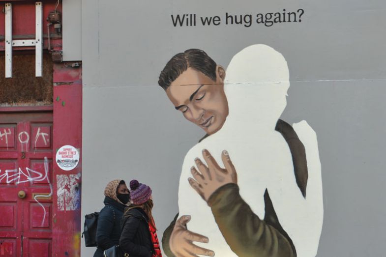 people walking past A mural 'Will we hug again?'