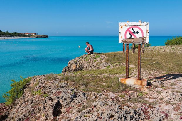 Man looking at the ocean next to a No Swimming sign