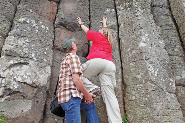 A man giving a women a leg up to climb a cliff