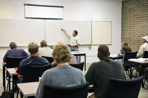 An adult education teacher pointing to an electrical circuit on the board. Focus on the diagram of the circuit.