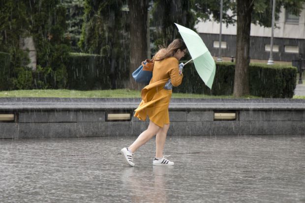 Belgrade One young woman running under umbrella in the sudden heavy spring windy rain in the city park , holding a bottle of water