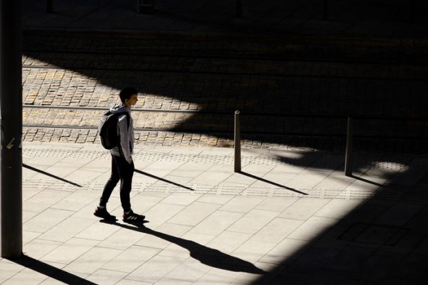 Belgrade, Serbia - October 26, 2020 One teenage boy standing alone waiting for a tram on bus stop in sunlight, high angle view from behind, with shadows