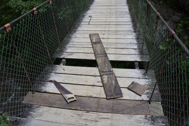 A wooden bridge with missing planks, symbolising precarity