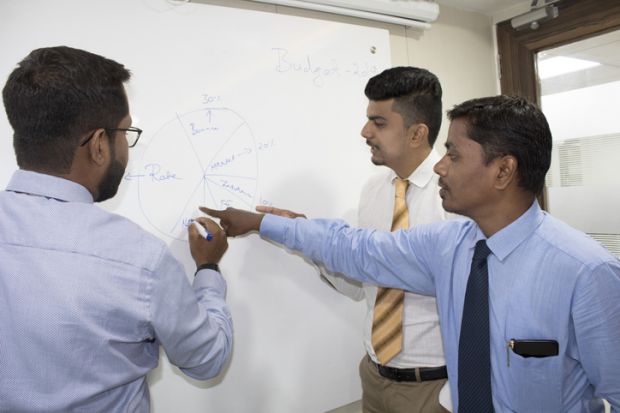 Indian business academics discuss a theory on a whiteboard