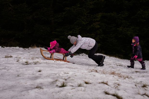 Captured during the New Year holidays in the Beskydy mountain in the north east of the Czech republic, young family is enjoying sledging on partly grassy meadow.