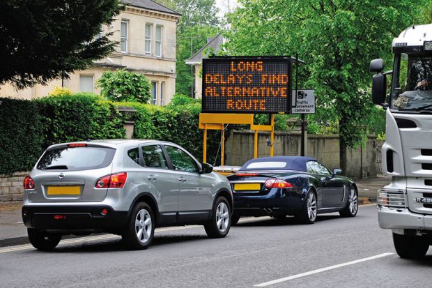 Cars in traffic jam with 'Long delays, find alternative route' sign
