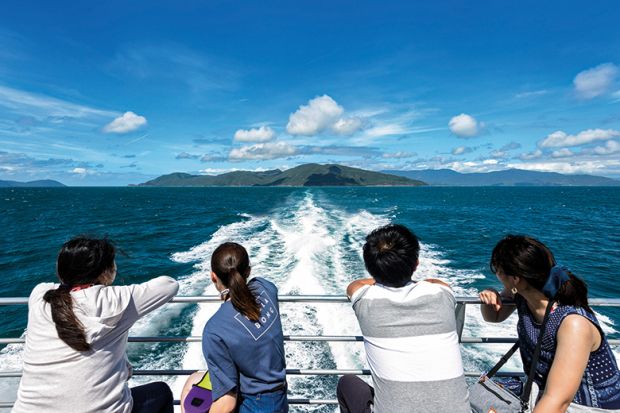 Chinese tourists looking back at the boat wake while cruising at the Great Barrier Reef, Far North Queensland, Australia. To illustrate declining research collaboration between China and Australia