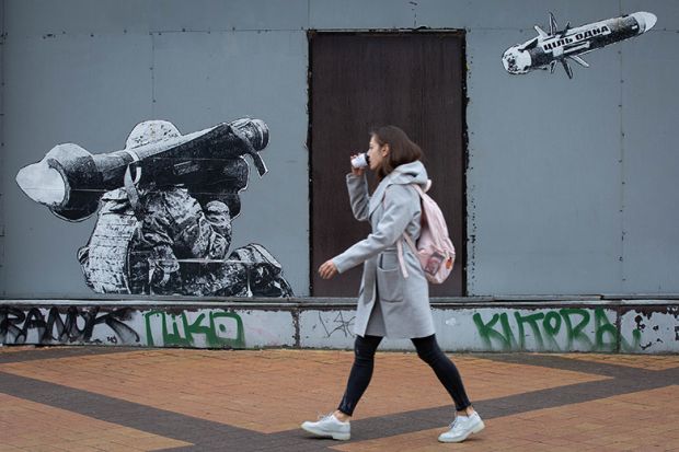A woman passes by graffiti depicting a Ukrainian serviceman making a shot with a US-made Javelin portable anti-tank missile system in central Kyiv