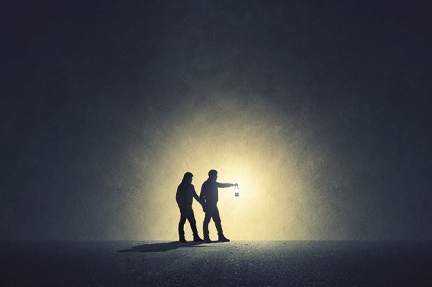 Two people walk in darkness with lamp illuminating their path