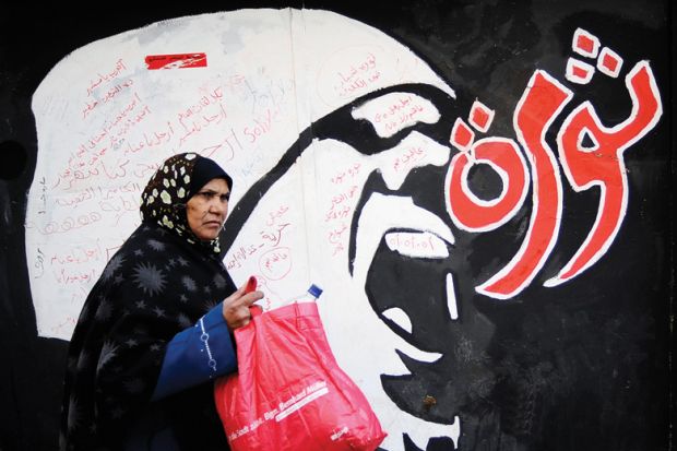 Egyptian woman walks past 'Revolution' graffiti, American University in Cairo