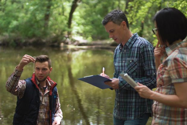 Three scientists examine lake water during fieldwork