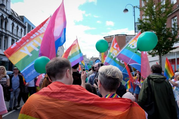 Gay Pride parade in Belfast, Northern Ireland, UK - September 5, 2017 - two people put their arms around each other under a rainbow flag as they march in the parade