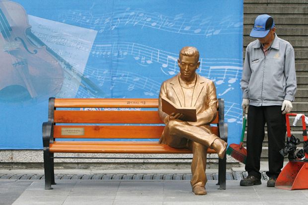 Man looks at sculpture of gold man on bench