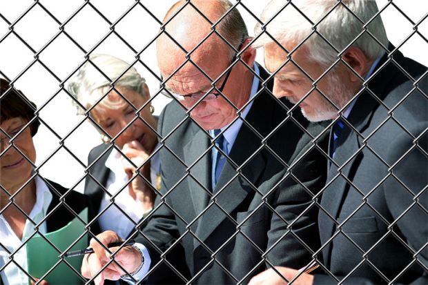 Group of academics in conversation behind chainlink fence