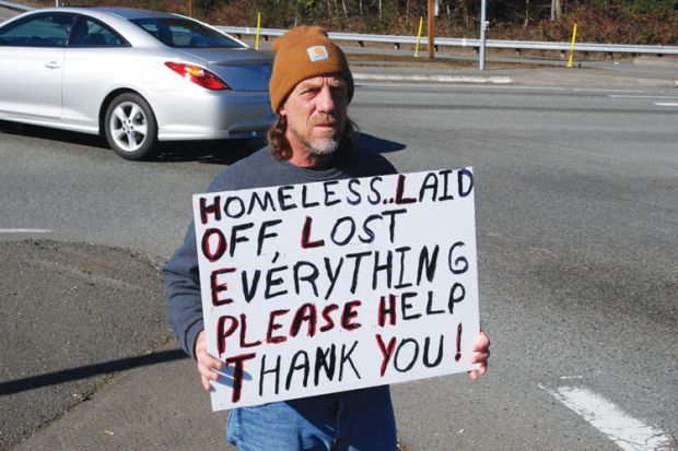 Homeless man on street corner holding sign