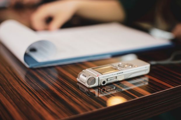 A tape recorder sits next to a pad of paper on a desk