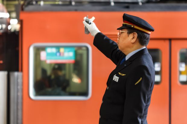 Unidentified Japanese train conductor gives a hand sign to a train while making a stop at Osaka Station.