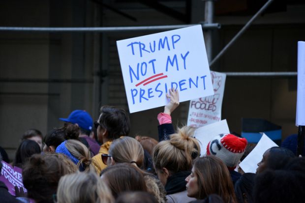 Someone in a crowd holds up a sign saying 'Trump - not my president'