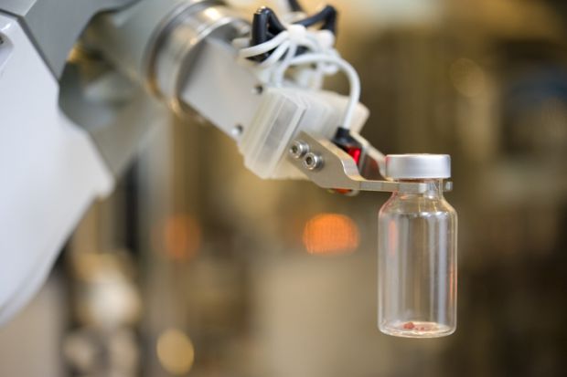 Robot hand picks up glass bottle in lab