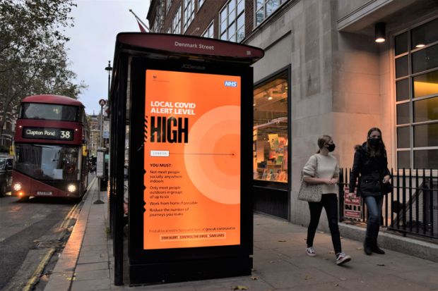 London, United Kingdom - October 30 2020 People with face masks walk past a Local Covid Alert Level High sign in Central London. The UK government has introduced a new three-tier system with restrictions increasing depending on the levels in each area.