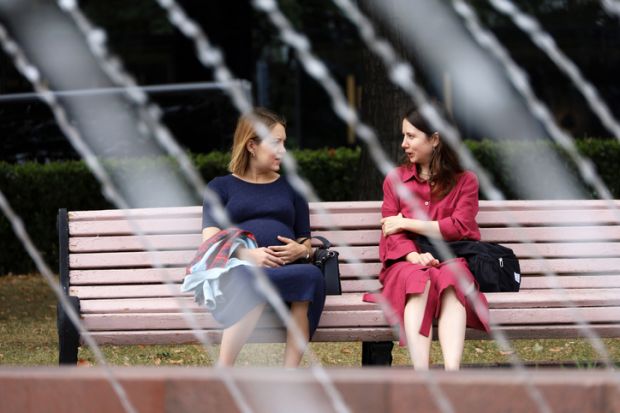 Moscow, Russia - August 2022 Two women talking while sitting on wooden bench in Moscow park, hot weather in summer city