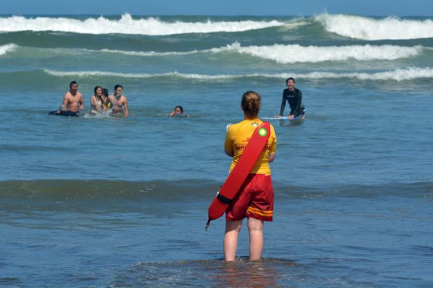 Muriwai, New Zealand - January 2 2015 New Zealand woman Lifeguard on duty watches swimmers in the sea.
