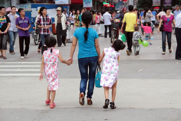 Nanchang, China, June 02, 2012 Colour photograph of a street in Nanchang, Jiangxi Province China. In the centre os the picture is a mother dressed in a blue t-shirt top and jeans with her hair tied back she is holding hands with two little girls dressed i