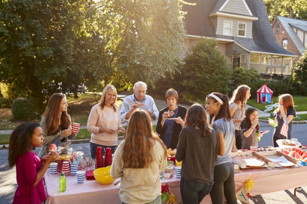 Neighbours talk and eat around a table at a block party representing collaboration between neighbouring universities