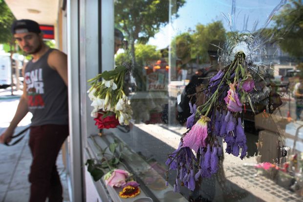 Flowers fill bullet holes in the windows of the IV Deli on May 25, 2014 in Isla Vista, California, after Elliot Rodger’s murderous rampage