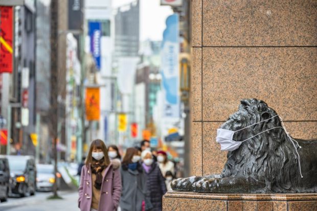 pedestrians walking past masked statue Tokyo