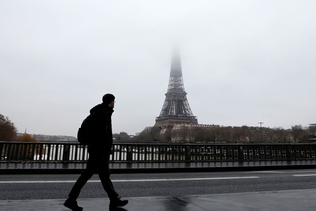 A man walks on a bridge across the Seine with the Eiffel Tower in the background