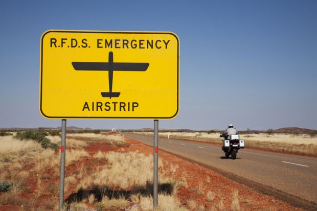Sign for Royal Flying Doctor Service emergency runway (on the road) in outback Western Australia, motor cyclist just passing