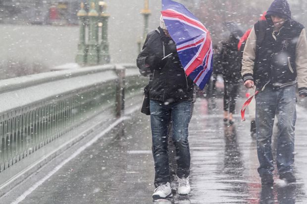 Man crosses bridge with Union Jack umbrella as snow falls