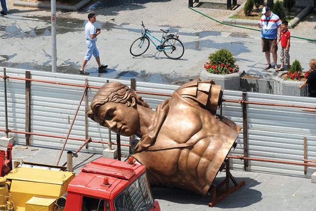 People walk past a bronze component of a statue