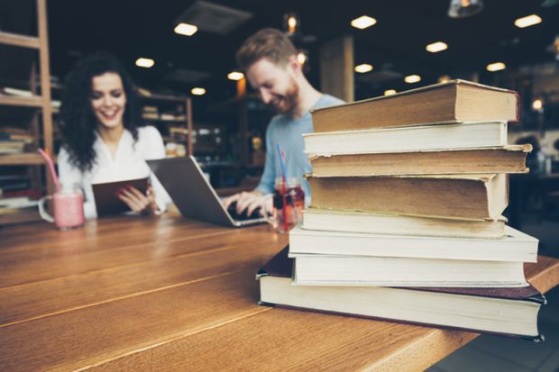 Students sitting at a table alongside a pile of books