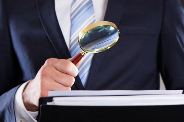 Suited businessman examining paperwork with magnifying glass