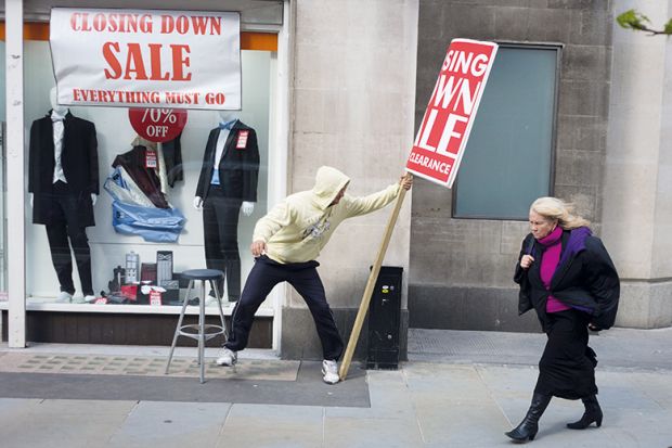 During a windy afternoon, a sandwich board man holds on to his sign advertising for a menswear shop's closure sale in central London