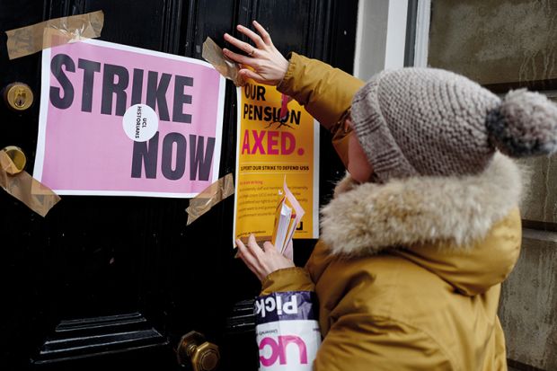 A demonstrator sticks a poster to a door as members of the University and College Union (UCU) stand at a picket line in protest against university lecturers' pay and pensions, outside of an entrance at University College London (UCL) in central London