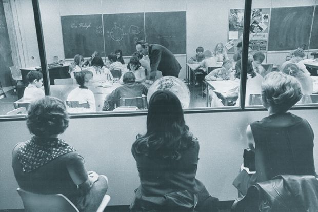 Three visiting teachers watch through a one-way window along the wall of a special demonstration classroom